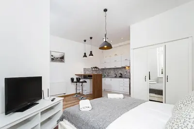 a white bedroom with a large bed and a kitchen at Charming Studio - 54 Starowislna street in Kraków