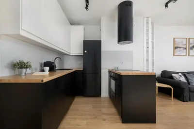 a kitchen with black cabinets and a living room at Mogilska Apartments with Parking near TAURON Arena Kraków by Noclegi Renters in Kraków