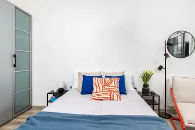 a white bedroom with a bed with blue and orange pillows at ICE Art by Cozyplace in Kraków