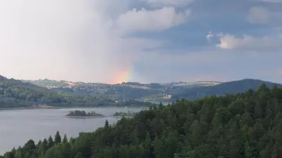 a rainbow in the sky over a lake with trees at DOMEK W HORTENSJACH in Mucharz
