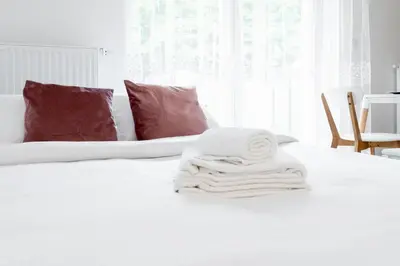 a pile of towels sitting on a white bed at Czerwone Maki Studio with Garden by BookingHost in Kraków