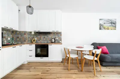 a kitchen with white cabinets and a table and a couch at Czerwone Maki Apartment with Garden by BookingHost in Kraków