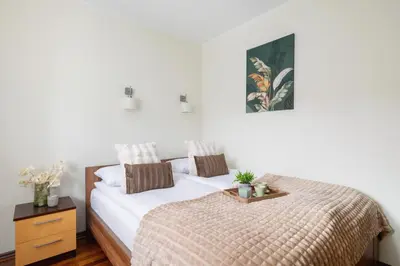 a white bedroom with a bed and a night stand at Cracow Verdant Apartment with Parking by Noclegi Renters in Kraków