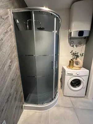 a glass shower in a bathroom with a washing machine at Apartament Mazowiecka 11 in Kraków
