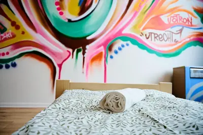 a bed with a pillow on it with a painting on the wall at Hostel Graffiti in Kraków