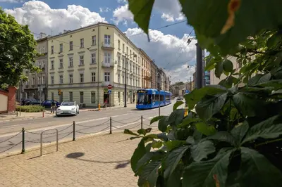 a blue bus driving down a city street with buildings at 1-Bedroom Apartment - Długa 65 Street in Kraków