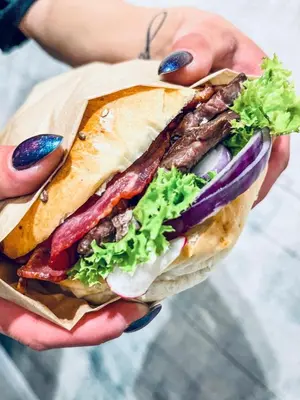 a person holding a sandwich with meat and vegetables at Rooftop Wawel view with jacuzzi l luxury apartment in Kraków