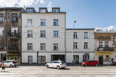 a white building with cars parked in a parking lot at Vintage Kalwaryjska Apartment in Kraków