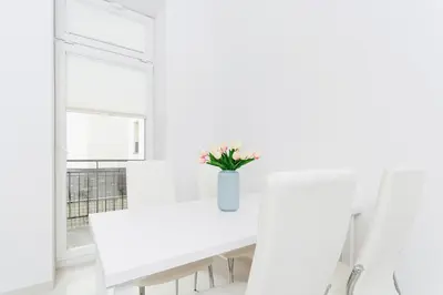 a white dining room with a white table and a vase of flowers at Two Bedroom Apartment - Rzeszowska 8 Street in Kraków
