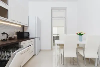 a white kitchen with a table and white chairs at Two Bedroom Apartment - Rzeszowska 8 Street in Kraków