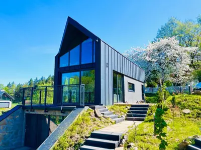a house with glass doors and stairs next to a river at U Boku Stoku - Domki w Kasinie in Kasina Wielka