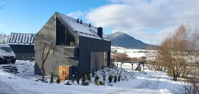 a small black house in the snow with a mountain at U Boku Stoku - Domki w Kasinie in Kasina Wielka