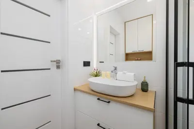 a white bathroom with a sink and a mirror at Elegancki Apartament w Krakowie z Klimatyzacją i Dostępem do Siłowni by Noclegi Renters in Kraków