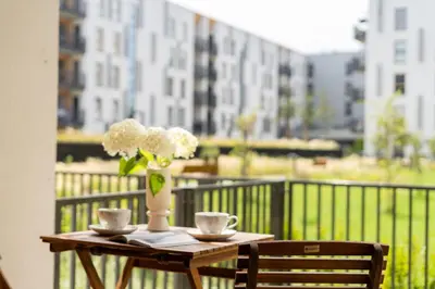 a table with two cups and a vase with flowers on a balcony at Lema Apartment near Tauron Arena in Kraków