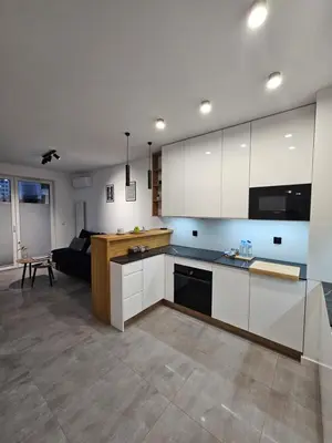 a kitchen with white cabinets and a living room at Apartament Centralna Park in Kraków