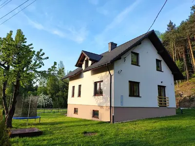 a white house with a black roof on a green field at Apartamenty pod groniem in Sułkowice