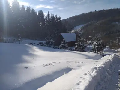 a snow covered yard with a house in the background at Domek za lasem in Laskowa