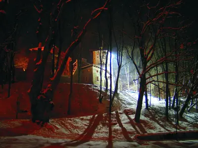 a snowy path in a forest at night with a building at Zamek Korzkiew in Korzkiew
