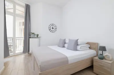 a white bedroom with a bed and a clock on the wall at Studio apartment with balcony - Starowiślna 41 in Kraków