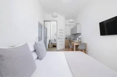 a white bedroom with a white bed and a tv at Studio apartment with balcony - Starowiślna 41 in Kraków
