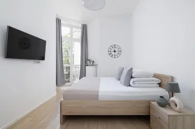 a white bedroom with a bed and a flat screen tv at Studio apartment with balcony - Starowiślna 41 in Kraków