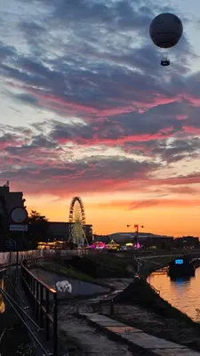 a hot air balloon flying over a ferris wheel at sunset at New Apartment Macedońska in Kraków