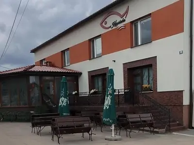 a building with chairs and umbrellas in front of it at Karpiówka noclegi in Osiek