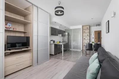 a living room with a couch and a tv and a kitchen at Apartament w Spokojnej Okolicy z Parkingiem by Noclegi Renters in Kraków