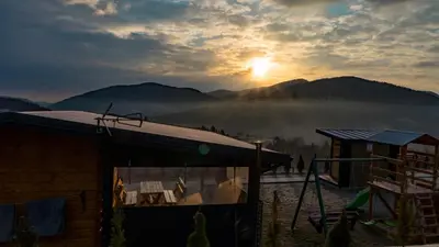 a house with the sun setting in the mountains at Domki- Limanowa domek 3 domek z jacuzzi i sauną in Limanowa