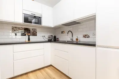 a white kitchen with white cabinets and black counter tops at Apartamenty FIGARETTI in Kraków