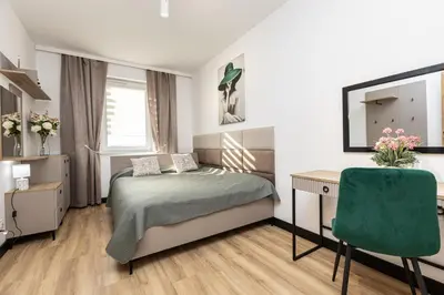 a bedroom with a bed and a desk and a green chair at Apartamenty FIGARETTI in Kraków