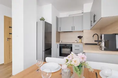 a kitchen with white cabinets and a wooden table with flowers at Nowoczesny Apartament w Krakowie z Klimatyzacją i Parkingiem by Noclegi Renters in Kraków