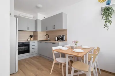 a kitchen with white cabinets and a wooden table and chairs at Nowoczesny Apartament w Krakowie z Klimatyzacją i Parkingiem by Noclegi Renters in Kraków