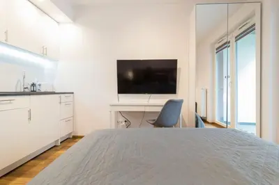 a white bedroom with a bed and a desk with a television at Zabłocie Charming Studio A in Kraków
