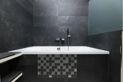 a bathroom with a white tub and black tiles at Aparthotel Miodowa 25 in Kraków