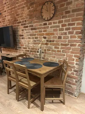 a wooden table with four chairs and a clock on a brick wall at Cracovia Kazimierz Historic Heart Accessible Apartament in Kraków