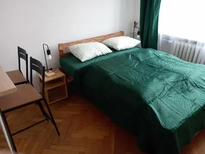 a bedroom with a bed with a green comforter and a chair at TomTom Hostel in Kraków