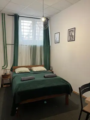 a bedroom with a green bed with a window at TomTom Hostel in Kraków