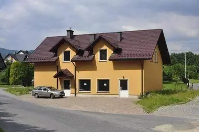 a yellow house with a car parked in front of it at Świnna Poręba Rooms in Świnna Poręba