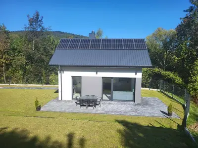a small white house with solar panels on the roof at Domek Całoroczny in Stróża