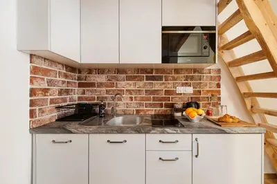 a kitchen with white cabinets and a brick wall at Apartamenty przy Kładce- Kazimierz Old Town in Kraków