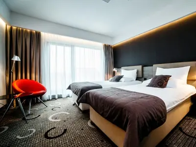 a hotel room with two beds and a red chair at Q Hotel Plus Kraków in Kraków