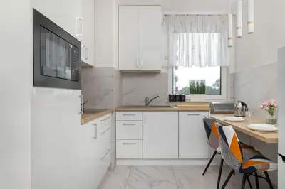 a kitchen with white cabinets and a table and chairs at Cozy Apartments Łaszkiewicza with Parking by Noclegi Renters in Kraków