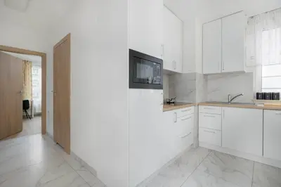 a kitchen with white cabinets and a tv on the wall at Cozy Apartments Łaszkiewicza with Parking by Noclegi Renters in Kraków