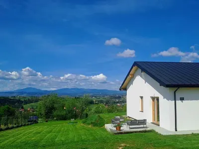 a white house with a blue roof on a green field at Leśna24 in Rabka-Zdroj