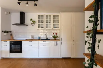 a white kitchen with white cabinets and wooden floors at GREEN OASIS - free parking, big balcony, private park in Kraków