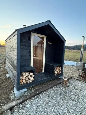 a black out house with a pile of fire wood at Domek na Odludziu - Tiny House in Spytkowice