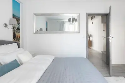 a white bedroom with a bed and a mirror at Apartament Szary in Kraków