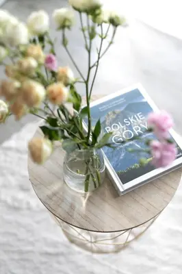 a glass vase with flowers and a book on a table at Apartament Szary in Kraków
