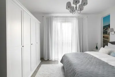 a white bedroom with a bed and a window at Apartament Szary in Kraków